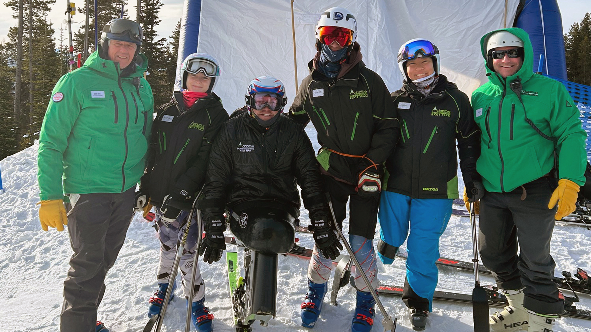 Four skiers, one of which is a mono-skier, stand facing the camera with a coach on either side .