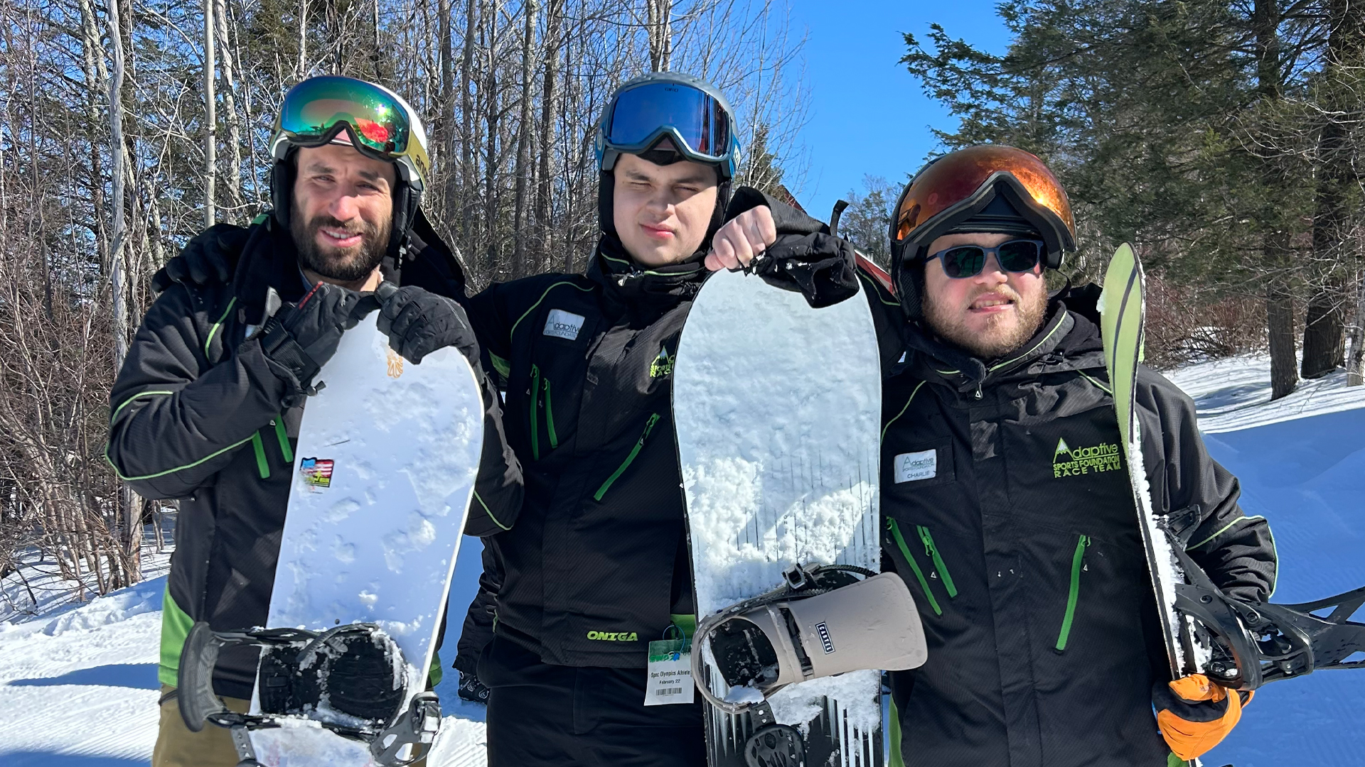 Three individuals stand holding snowboards