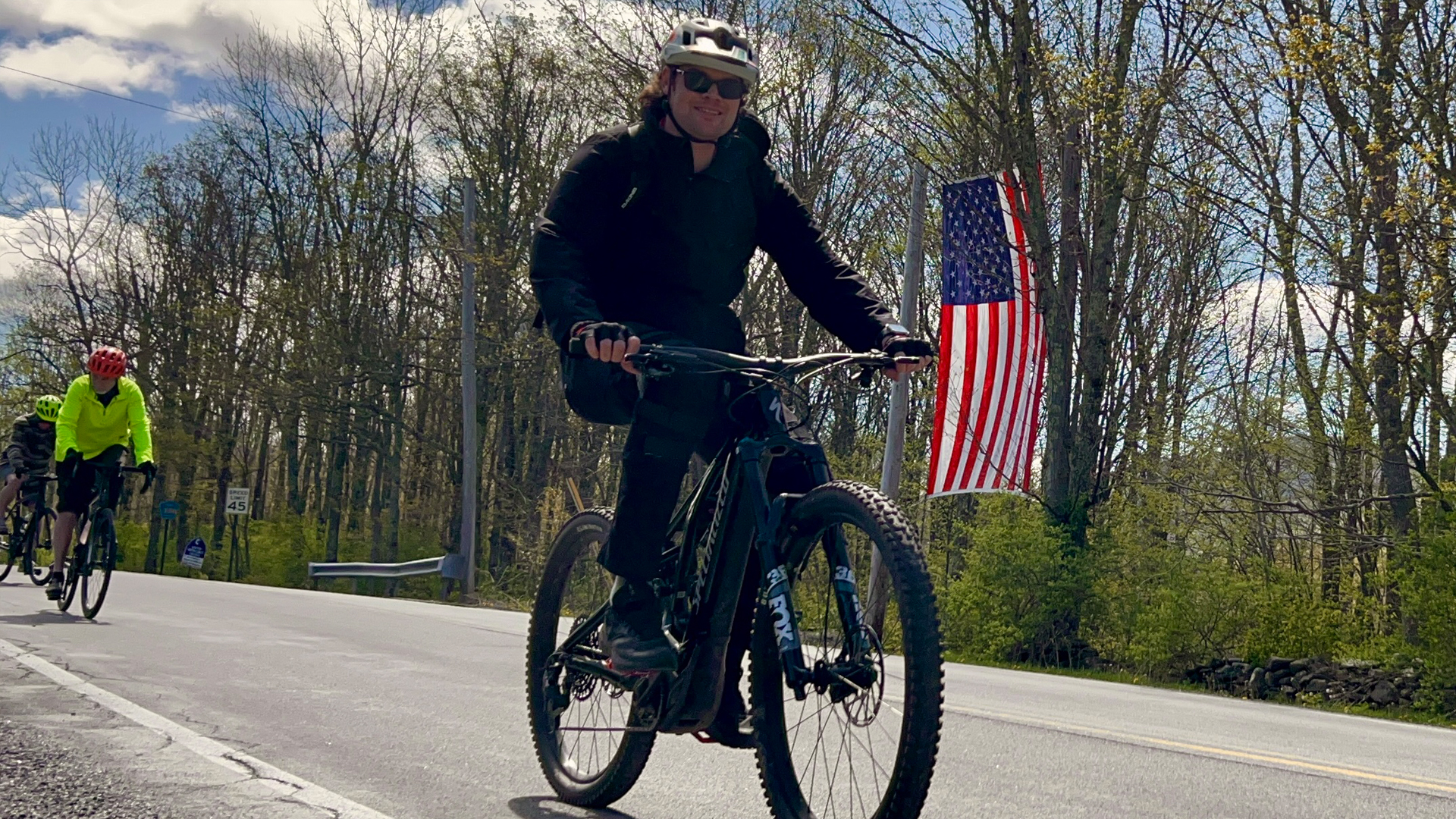 Man smiling on bicycle with American flag behind him